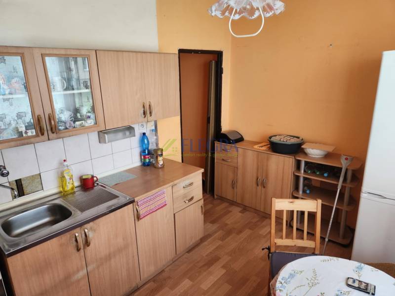 Küche in einer Einzimmerwohnung mit Holzschränken, Tisch und Kühlschrank.