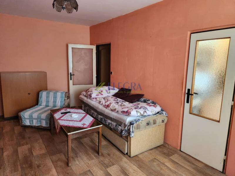 Ein Zimmer in einer Einzimmerwohnung mit einem Bett, einem Sessel und einem Tisch auf einem Parkettboden.