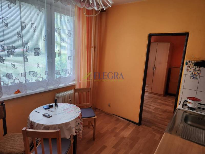 Küche in einer Einzimmerwohnung mit Tisch, Stühlen und Vorhängen am Fenster.