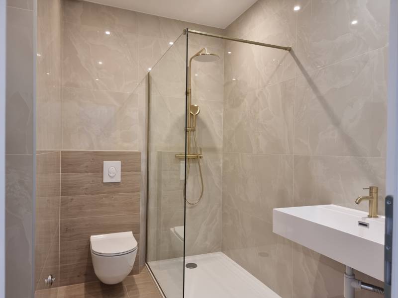 Badezimmer in einer 4-Zimmer-Wohnung mit Dusche, Toilette und Waschbecken, helle Fliesen.