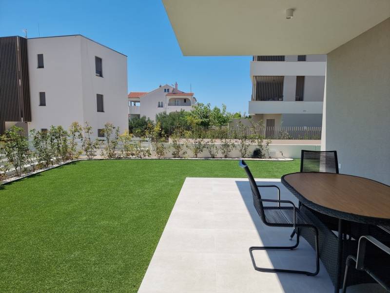 Garten einer 4-Zimmer-Wohnung in Vodice mit Terrasse und modernem Tisch auf dem Rasen.