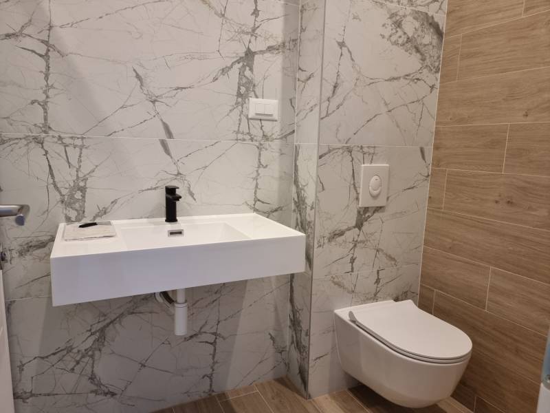 Badezimmer mit hängendem WC, Keramikwaschbecken und Marmorfliesen in einer 4-Zimmer-Wohnung.