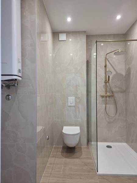 Badezimmer in einer 4-Zimmer-Wohnung mit Toilette, Dusche und glatten Fliesen.