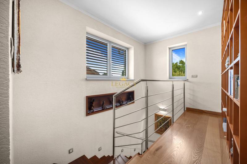 Holztreppe mit Metallgeländer, Bücherregal und Fenster in einem Einfamilienhaus.