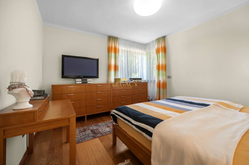 Schlafzimmer im Einfamilienhaus mit Holzmöbeln, Fernseher und bunten Vorhängen.