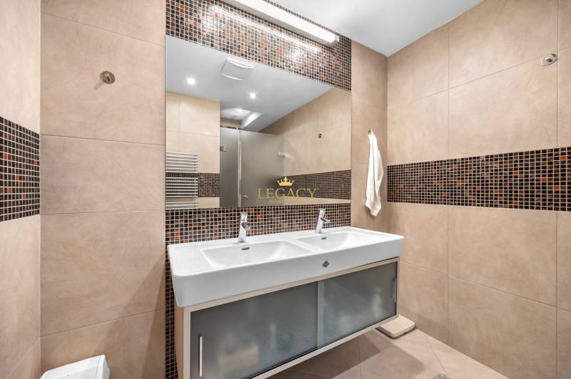 Badezimmer mit Doppelwaschbecken, braunen Fliesen und Spiegel in einem Einfamilienhaus.