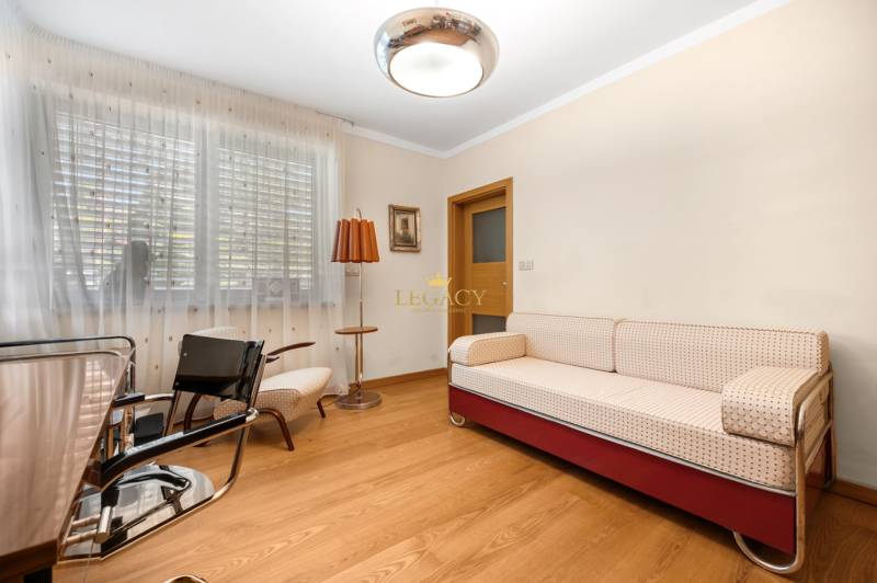 Ein Zimmer in einem Einfamilienhaus mit einem Sofa, Sesseln, einer Lampe und Holzboden.