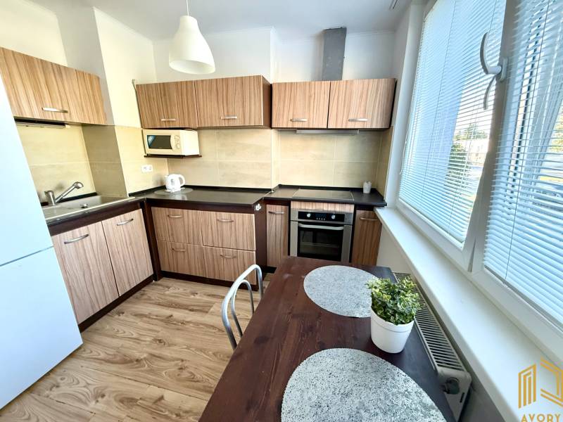 Küche in einer 2-Zimmer-Wohnung mit hellem Holz, weißen Geräten und einem Tisch.