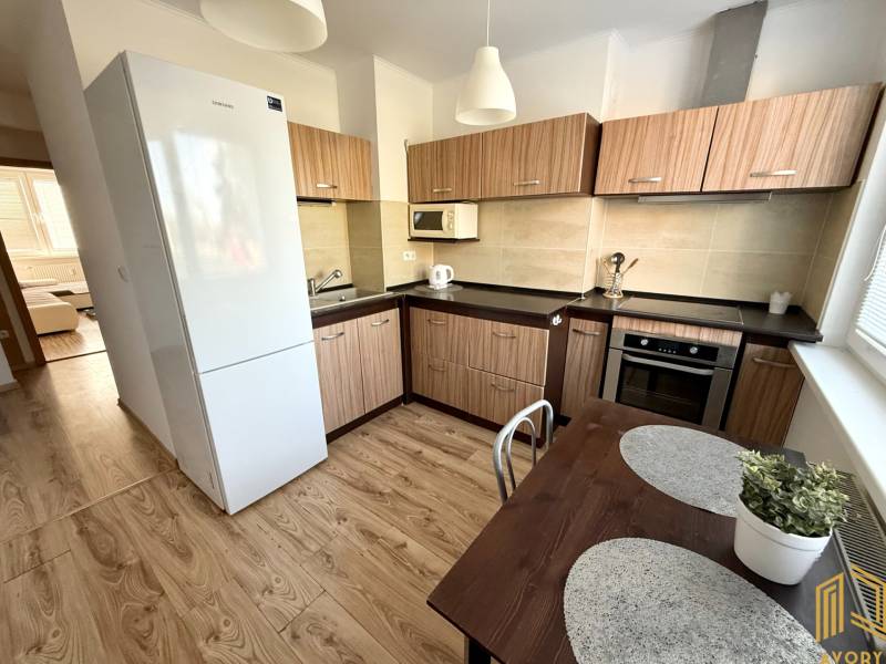 Küche in einer 2-Zimmer-Wohnung mit Holzmöbeln, einem weißen Kühlschrank und einem Esstisch.