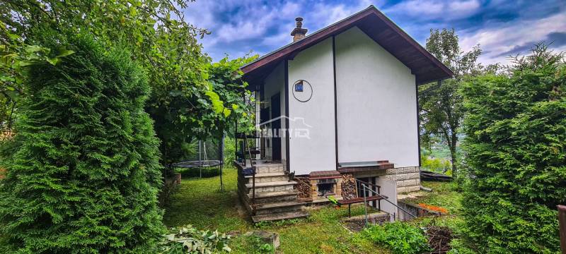 Eine Hütte in Mojša, umgeben von Grün, Treppen führen zum Eingang, ein Trampolin im Garten.