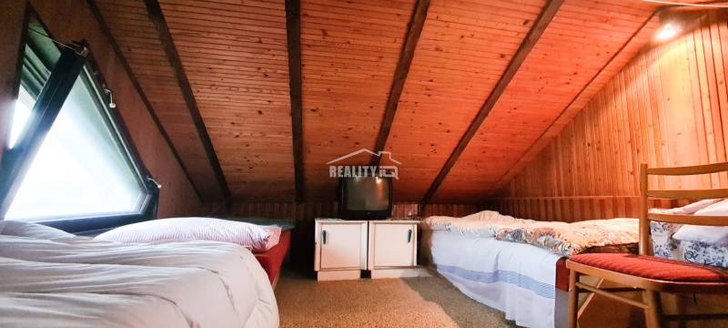 Dachboden-Schlafzimmer in einer Hütte mit Holzverkleidung, Betten und einem älteren Fernseher.