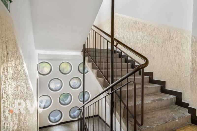 Treppe mit Geländer, runde Fenster, strukturierte Wände, räumliche Anordnung.