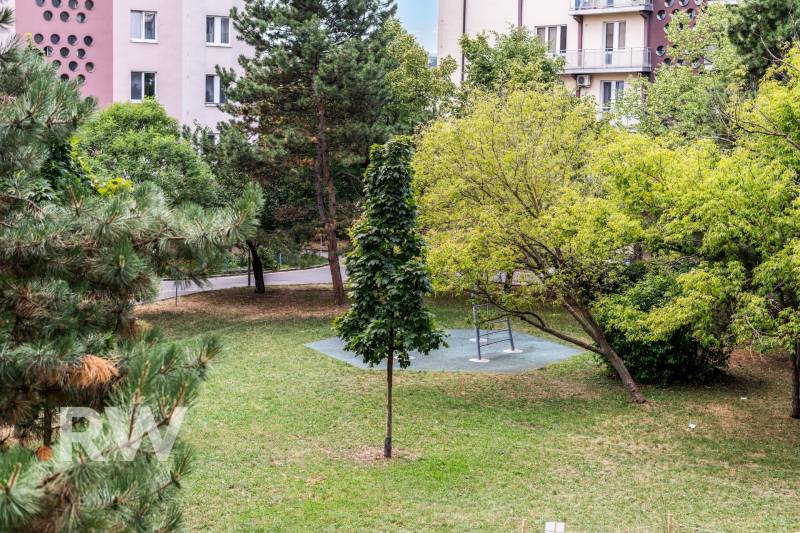 Park in Bratislava auf den Tschechoslowakischen Fallschirmjägern mit einer Bank und Grünflächen, umgeben von Wohnhäusern.