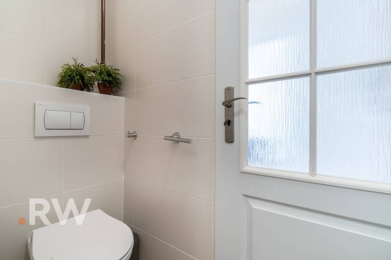Badezimmer einer Zweizimmerwohnung mit Toilette, Keramikfliesen und Glastüren.