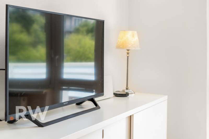 Ein Fernseher und eine Lampe auf einer weißen Kommode in einer Zweizimmerwohnung.
