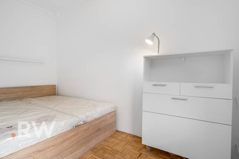 Schlafzimmer mit Bett und Kommode in einer 2-Zimmer-Wohnung, Boden mit Holzdekor.
