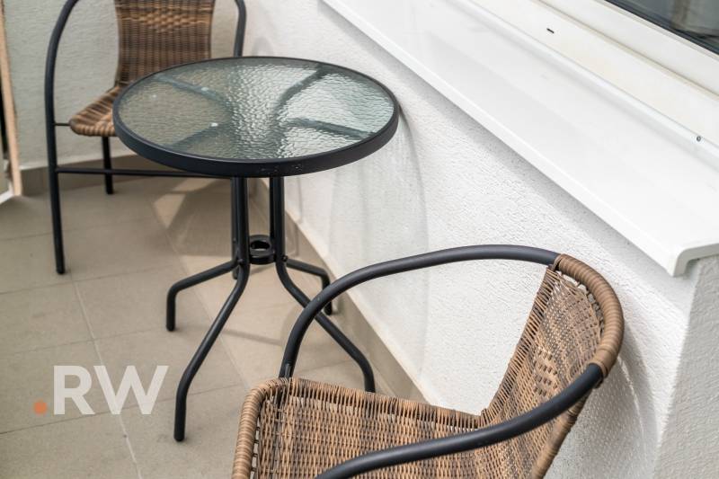 Balkon mit Rattanstühlen und Glastisch in einer 2-Zimmer-Wohnung.