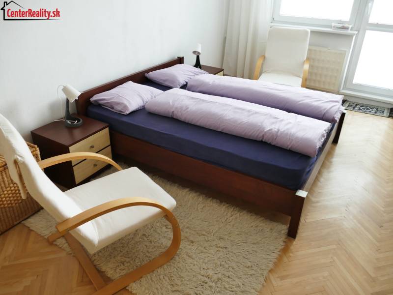Schlafzimmer in einer 3-Zimmer-Wohnung mit einem Doppelbett, bequemen Stühlen und einem hellen Teppich.