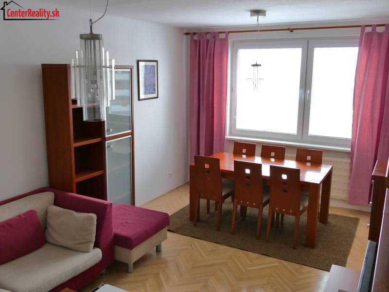Essbereich mit Holztisch in einer 3-Zimmer-Wohnung, ergänzt durch rosa Vorhänge und ein Sofa.