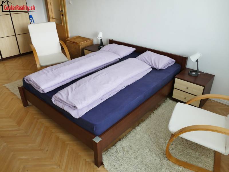Schlafzimmer in einer 3-Zimmer-Wohnung mit einem Holzbett, einem Stuhl und einem weißen Teppich.