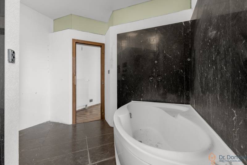 Badezimmer mit Eckbadewanne und schwarzen Fliesen, Holzboden in Geschäftsräumen.