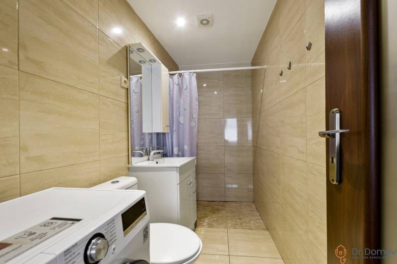 Badezimmer in einer 2-Zimmer-Wohnung mit Waschmaschine, Spiegel und Duschvorhang.