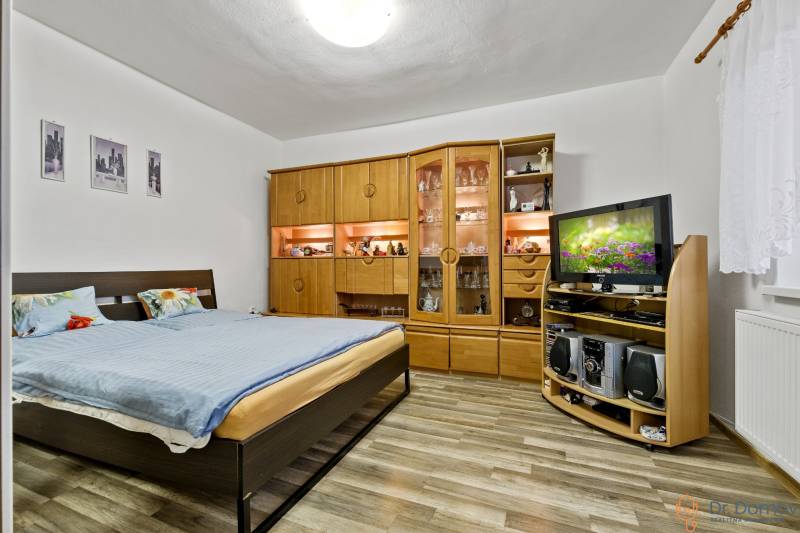 Schlafzimmer mit Doppelbett, Wohnwand aus Holz und Fernseher in einer Zweizimmerwohnung.