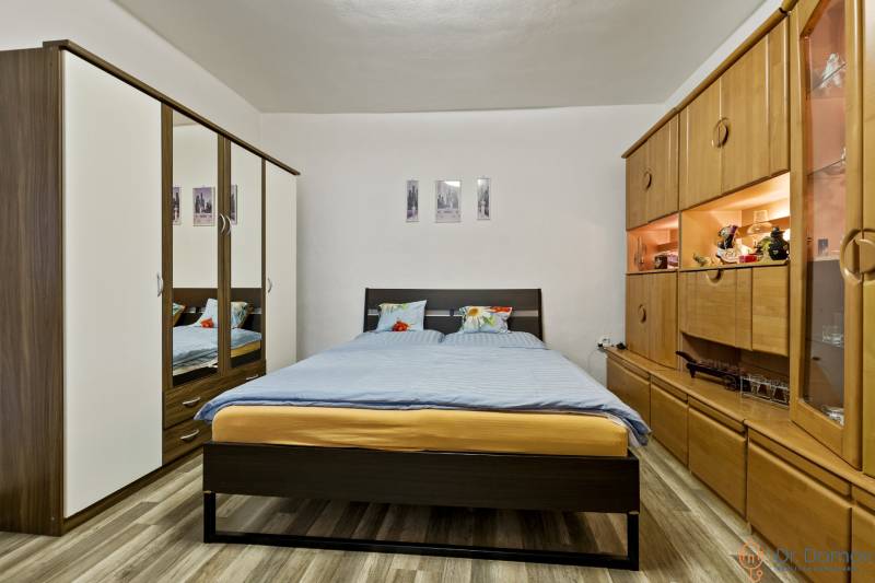 Schlafzimmer in einer 2-Zimmer-Wohnung mit Doppelbett, Einbauschrank und Holzwandmöbel.