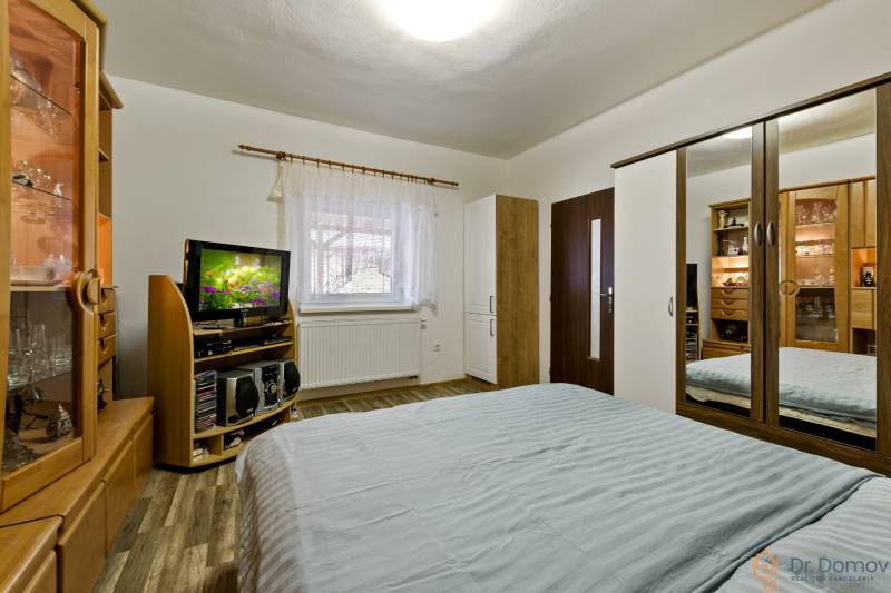 Schlafzimmer in einer 2-Zimmer-Wohnung mit Bett, Kleiderschrank, Fernseher und Holzmöbeln.