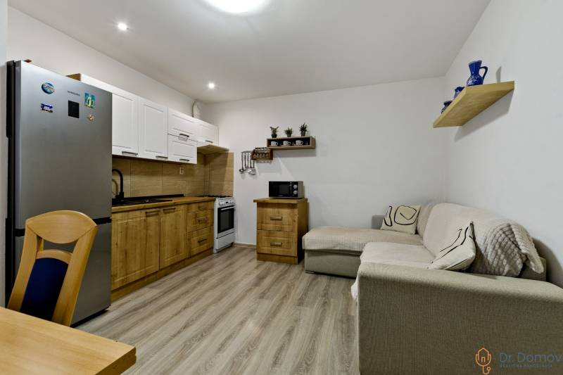 Offene Küche mit Holzschränken und Sofa in einer Zweizimmerwohnung.