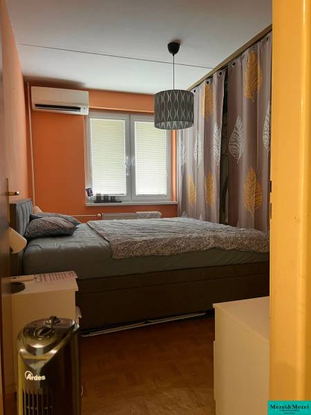 Schlafzimmer in einer 3-Zimmer-Wohnung mit Doppelbett, orangefarbenen Wänden und Klimaanlage.