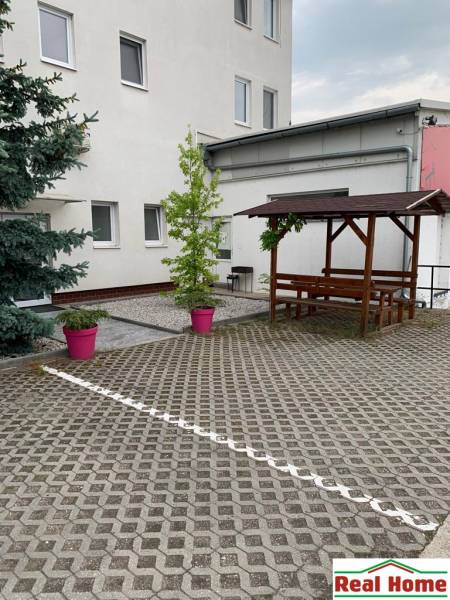 Palast mit Pflastersteinen, Holzsitzgelegenheiten und Pflanzen in rosa Blumentöpfen auf der Šamorínska-Straße.
