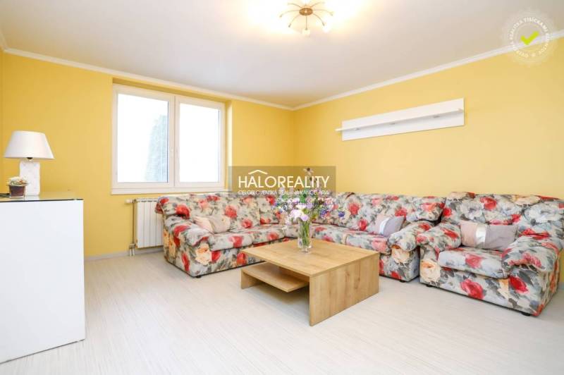 Gelbes Wohnzimmer mit einem geblümten Sofa und einem Holztisch in einer 2-Zimmer-Wohnung.