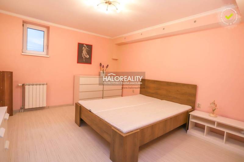 Schlafzimmer mit Bett in einer 2-Zimmer-Wohnung mit geräumiger Kommode und pastellrosa Wand.