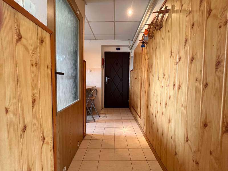 Holzverkleidung im Flur einer 2-Zimmer-Wohnung, helle Fliesen, klappbare Stühle.