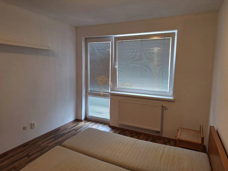 Schlafzimmer in einer Zweizimmerwohnung mit Bett und Fenster mit Jalousien.
