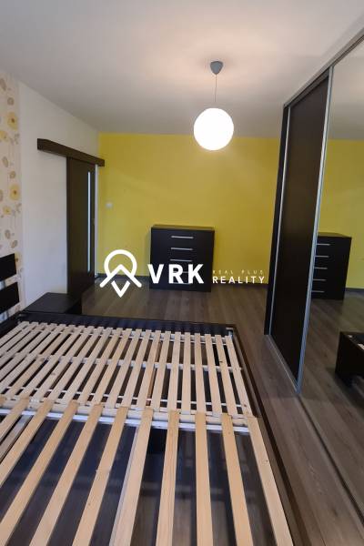 Schlafzimmer in einer 2-Zimmer-Wohnung mit Bett, zwei Kommoden und gelber Wand.