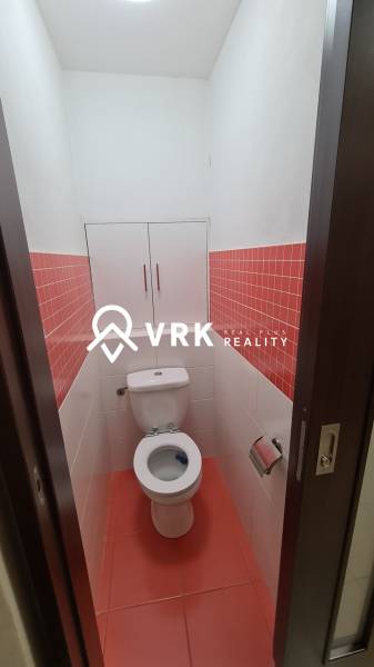 Toilette mit weißen Fliesen und einem Schrank in einer Zweizimmerwohnung mit roten Fliesen.