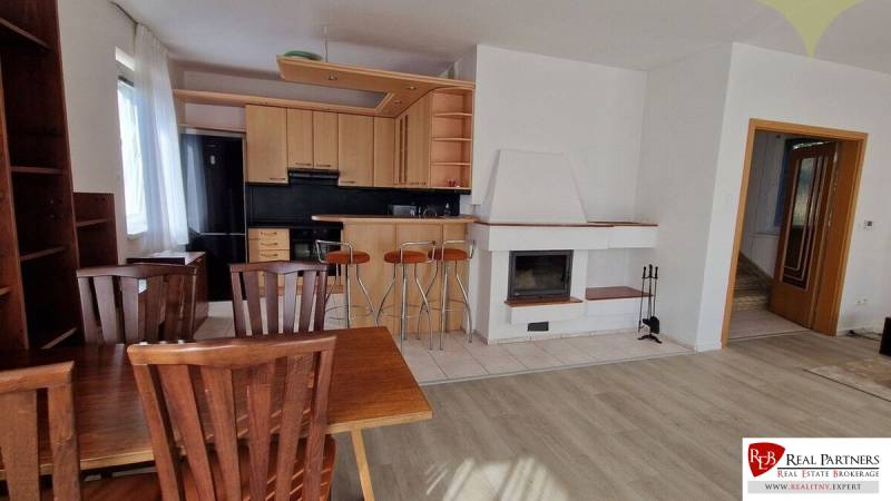 Wohnzimmer in einem Einfamilienhaus mit Kamin, Küche und Holzmöbeln.