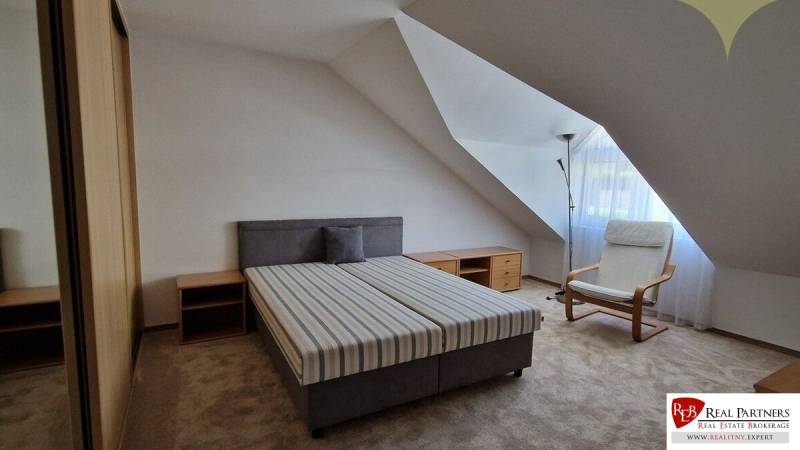 Schlafzimmer mit Bett und Sessel in einem Einfamilienhaus, helle Wände, schräges Dach.