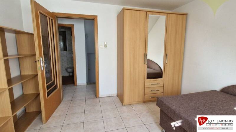 Zimmer in einem Einfamilienhaus mit Bett, Schrank, Regalen und Badezimmer.
