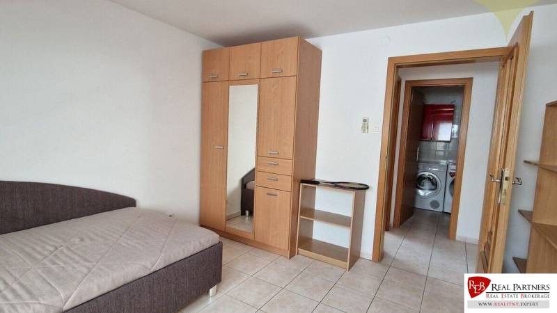 Ein Zimmer in einem Einfamilienhaus mit einem Bett, einem Schrank und einem Blick ins Badezimmer mit einer Waschmaschine.