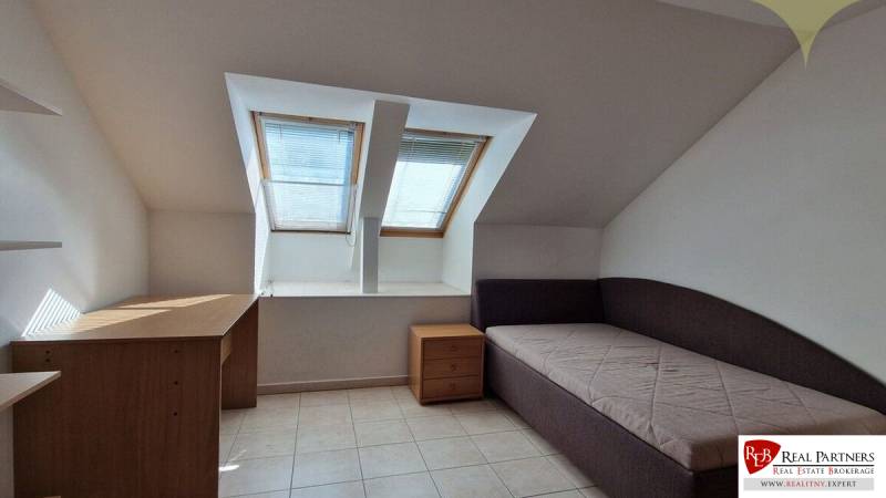 Ein Dachzimmer in einem Einfamilienhaus mit zwei Dachfenstern, einem Bett und einem Schreibtisch.