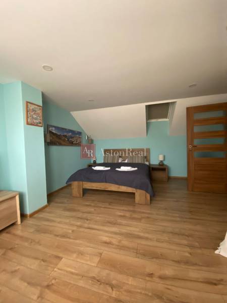 Einfamilienhaus: Schrägdach, Ehebett, Holzboden, blaue Wand und Nachttische.