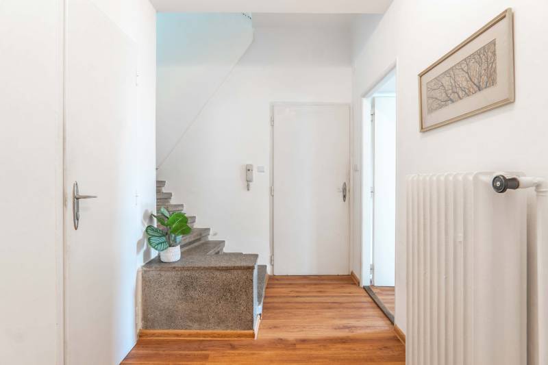 Flur mit Holzboden, Treppe, Bild und Heizkörper in einer 2-Zimmer-Wohnung.