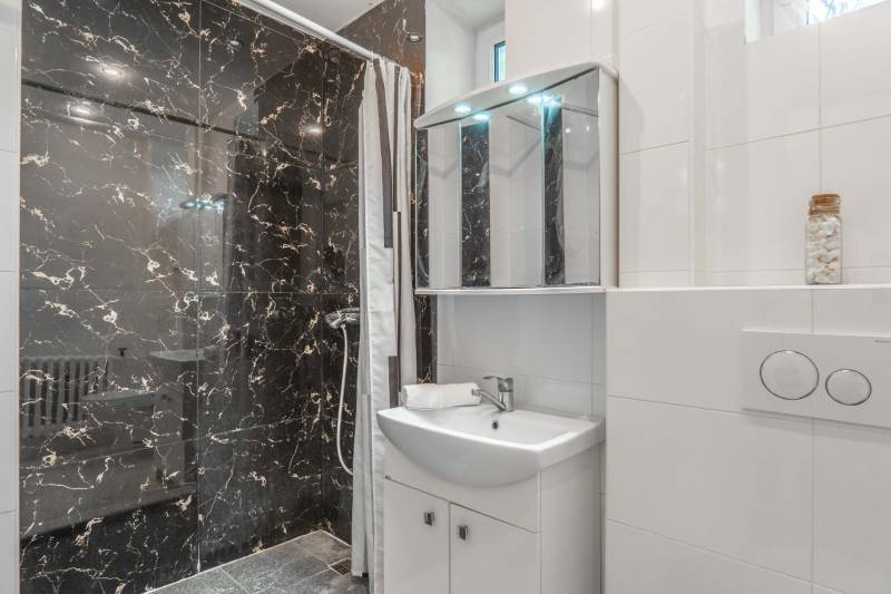 Badezimmer in einer 2-Zimmer-Wohnung mit dunklen Marmorkacheln und einer Duschkabine.