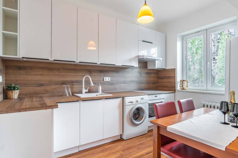 Küche mit großem Fenster, Esstisch, Waschmaschine und Holzverkleidung in einer 2-Zimmer-Wohnung.