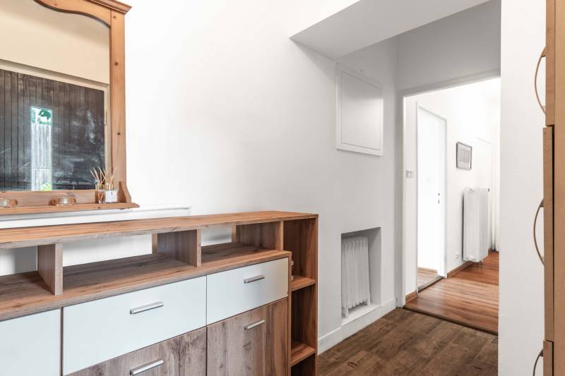 Kommode mit Holzspiegel im Flur einer 2-Zimmer-Wohnung, die zu einem hellen Korridor führt.