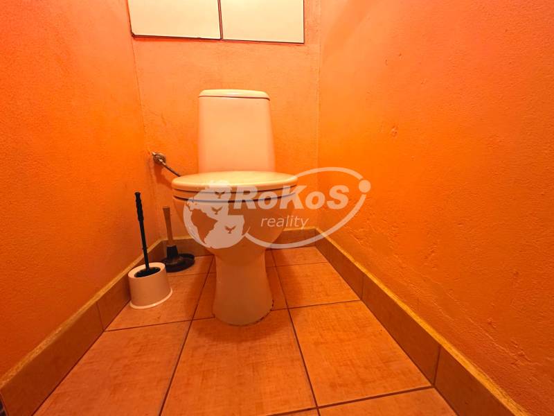 Oranges WC in einer 3-Zimmer-Wohnung mit einer Toilettenbürste in der Ecke des Raumes.