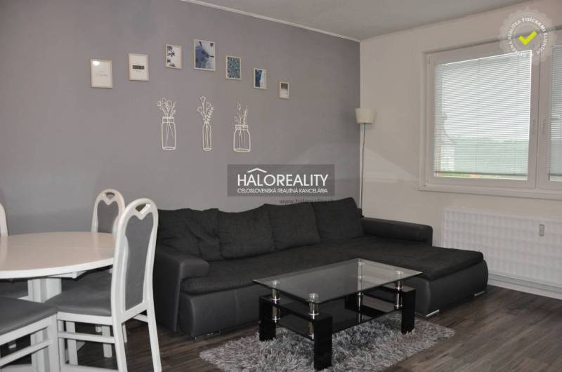 Wohnzimmer mit dunklem Sofa und Esstisch in einer 3-Zimmer-Wohnung, dekorative Bilder an der Wand.
